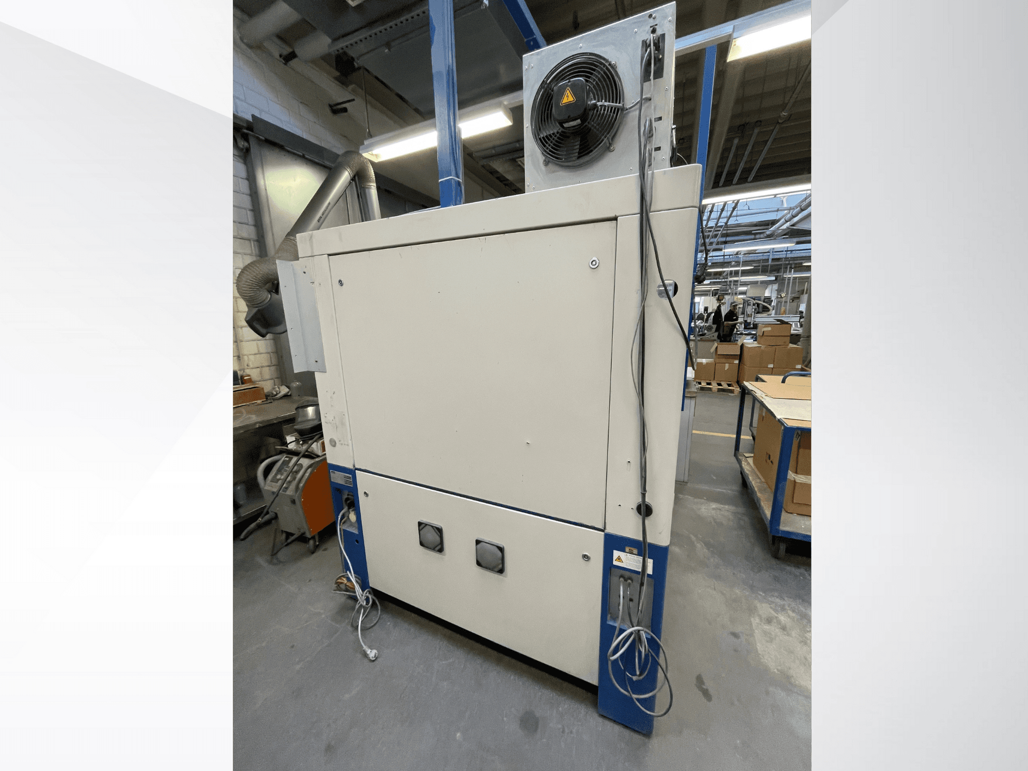Ipari szárítógép ventilátorral, oldalnézet; szellőztetéssel és több elektromos csatlakozóval rendelkezik. Márka/modell nem látható.