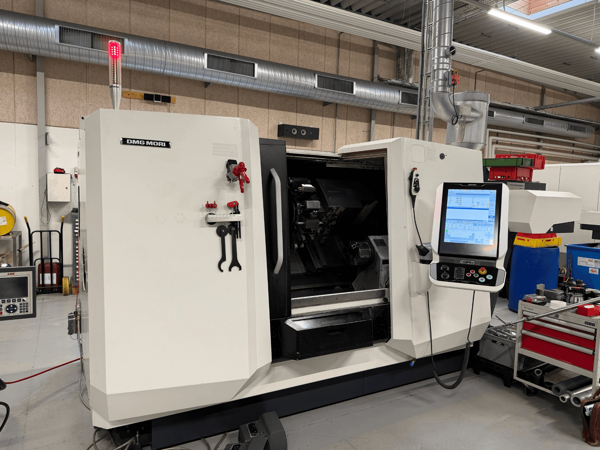 DMG MORI CLX 450 V6 vízszintes eszterga, elölnézet, amelyen látható a vezérlőpanel, a vészleállító gomb és a biztonsági lámpa.