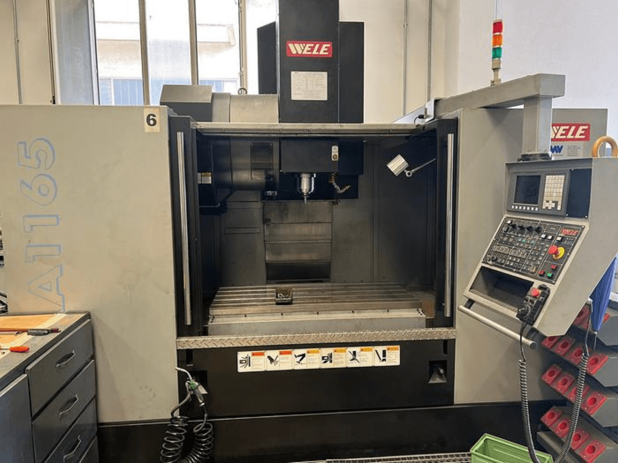 WELE A165 CNC megmunkálóközpont, előlnézet, a vezérlőpanel, a szerszámtartó és a munkaasztal látható. Ipari beállítás.
