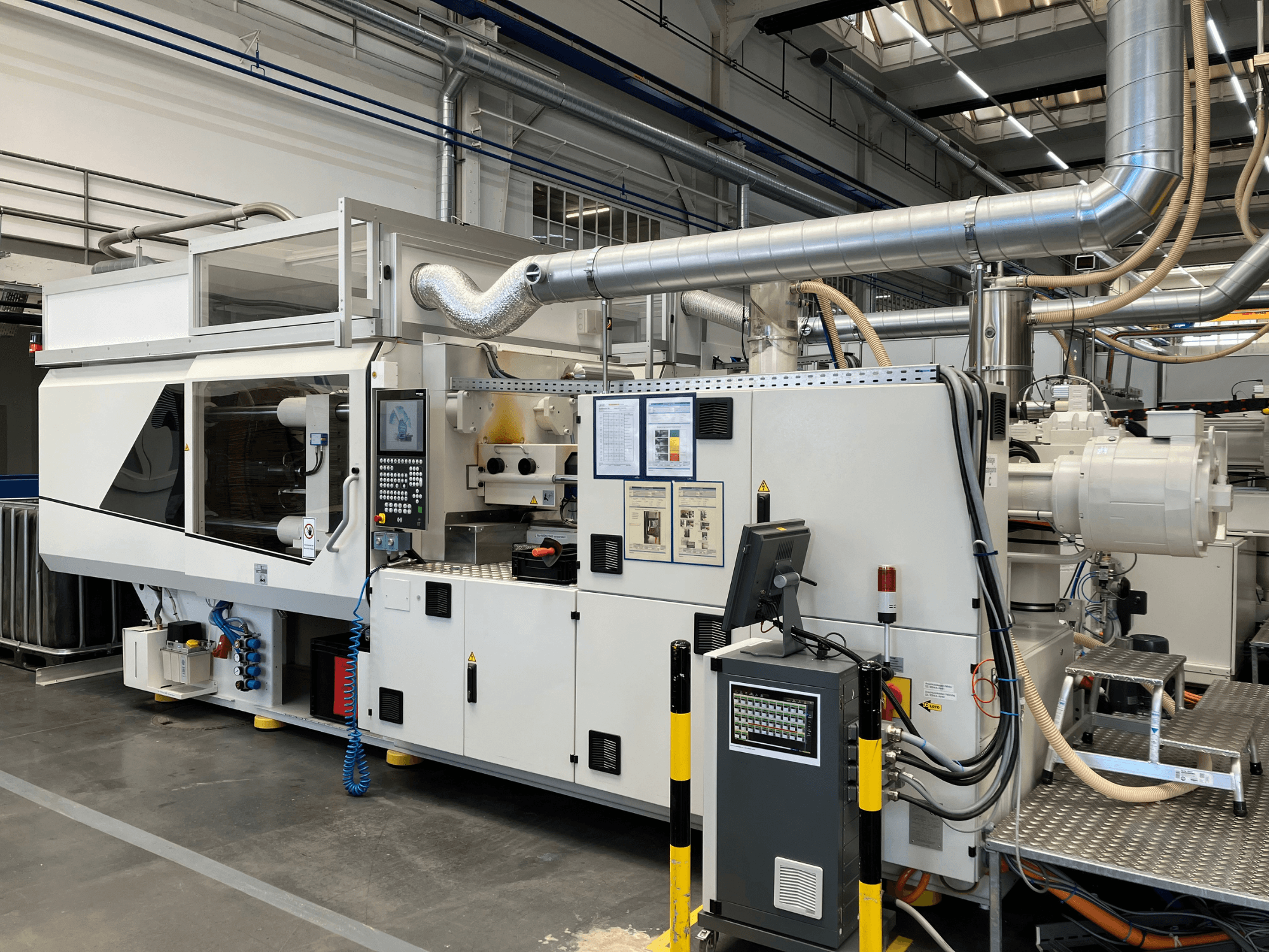 Egy ipari gép elülső nézete vezérlőpanellel, csövekkel és kijelző képernyőkkel, elegáns fehér dizájnnal és műszaki részletekkel.