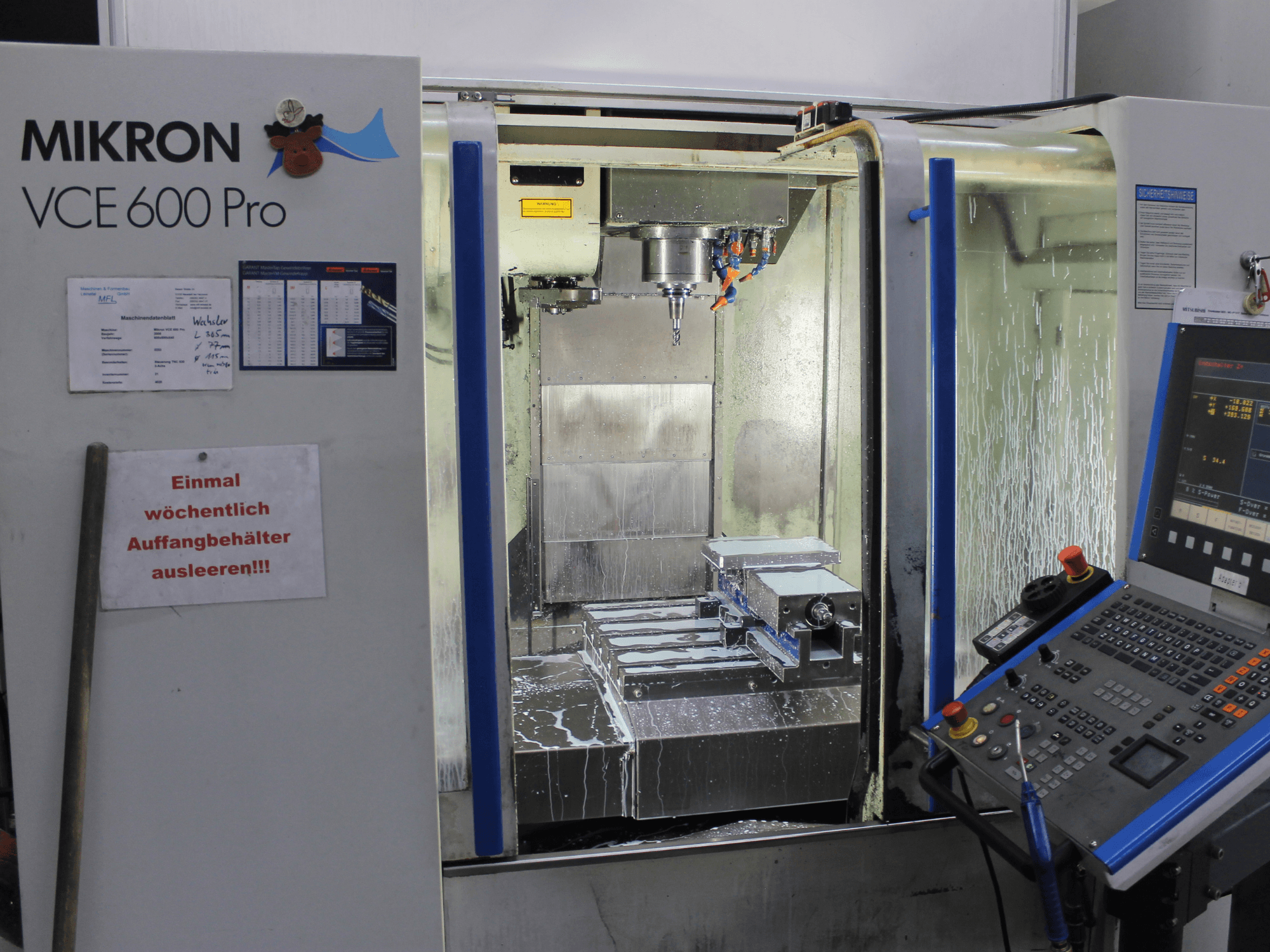 Mikron VCE 600 Pro megmunkálóközpont, előlnézet, vágószerszámokkal, hűtőfolyadék-fröccsel és gombokkal ellátott kezelőpanellel.