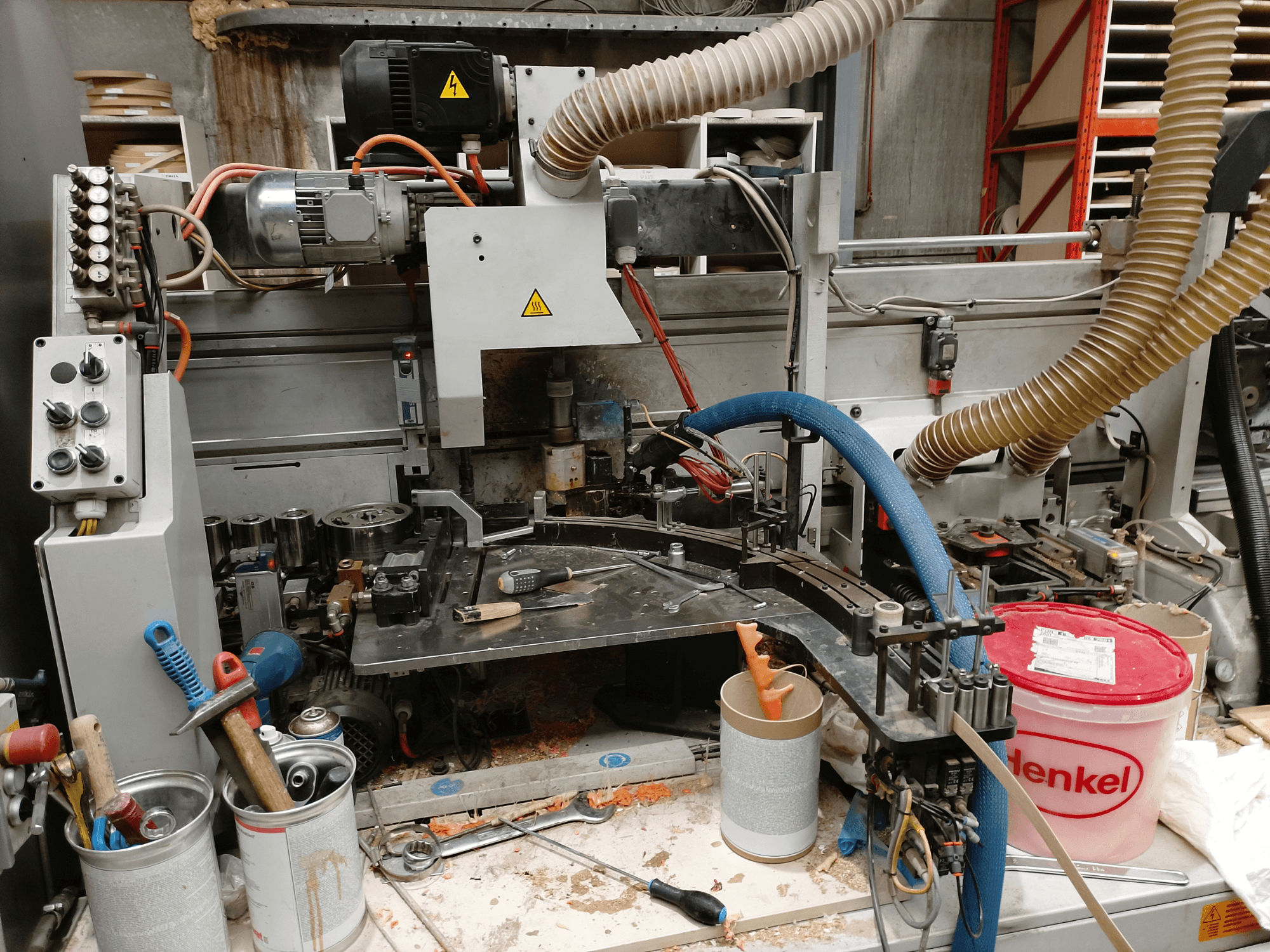 BIESSE Edge Stram B1 szegélyezőgép elölnézetben, a gépeket, tömlőket és munkaeszközöket mutatja a faforgácsok között.