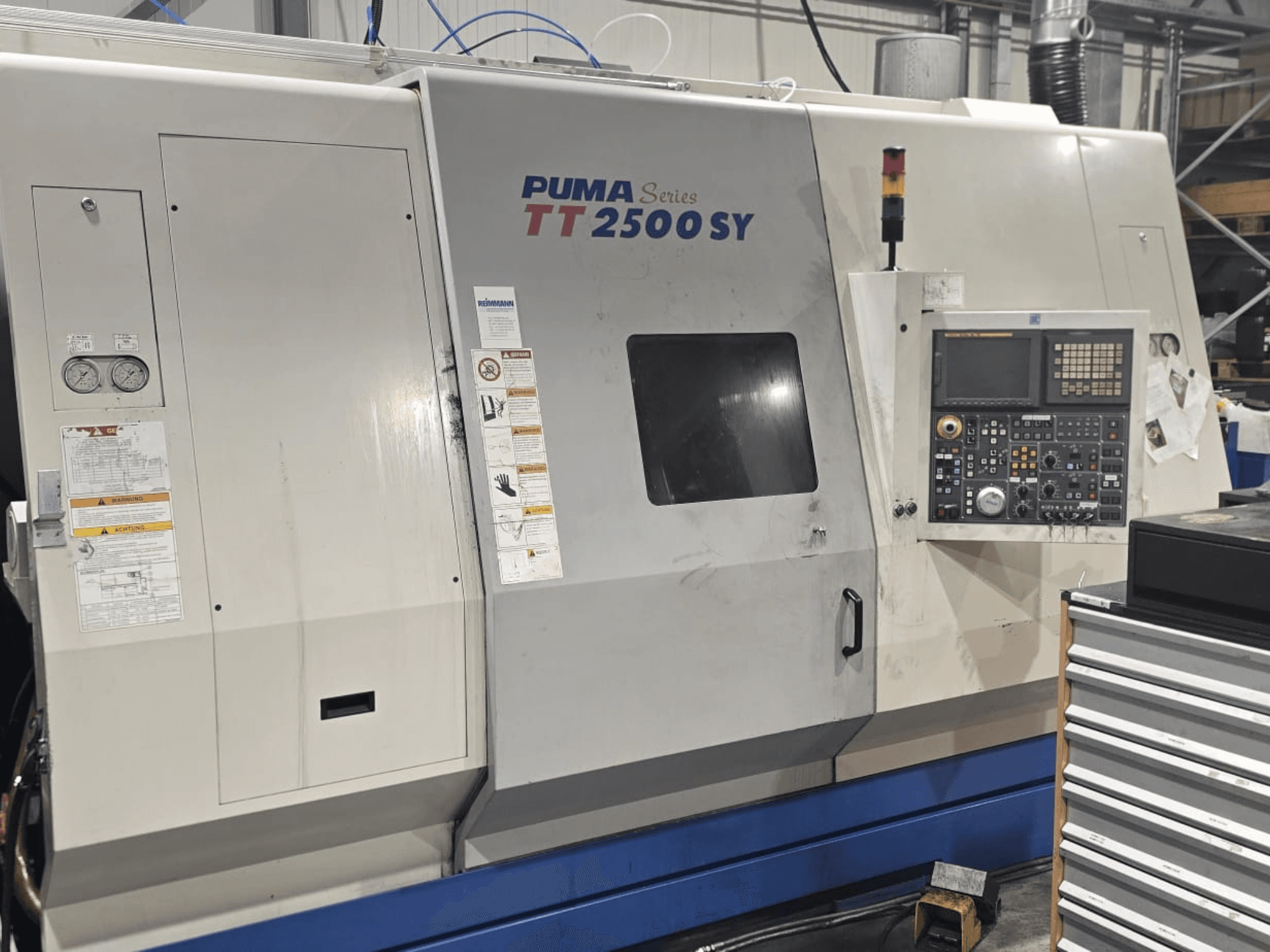 PUMA TT 2500 SY sorozatú CNC eszterga, előlnézet; a vezérlőpanel tárcsákkal és gombokkal, műszerekkel és a kezelési címkékkel látható.