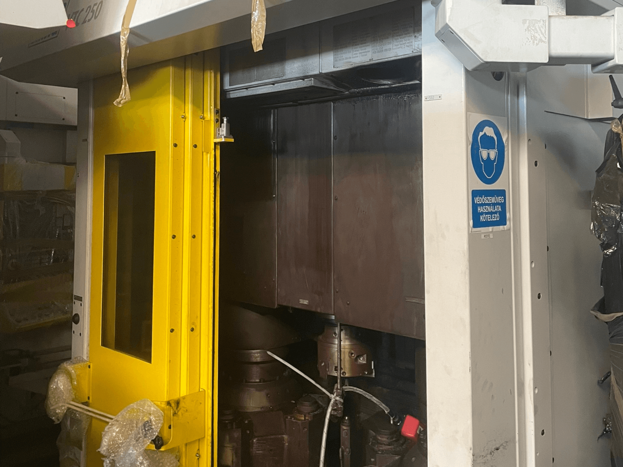 Sárga bejárati ajtó egy gép biztonsági táblával, egy Z250-es típusú ipari gép elülső nézete, a belső alkatrészeket mutatja.