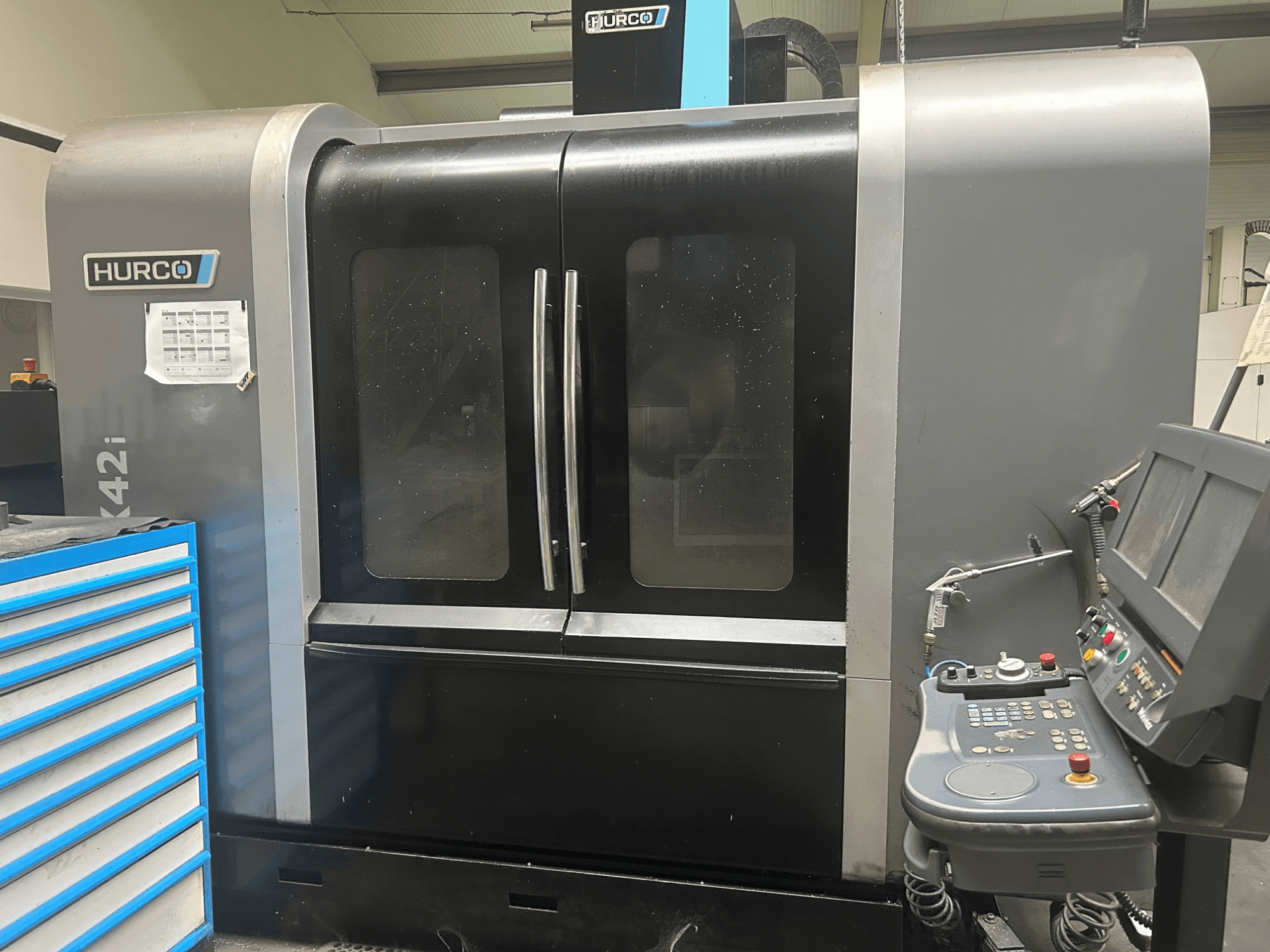 Hurco VMX42i CNC-gép, elölnézet az oldalsó vezérlőpanellel, dupla ajtókkal és látható műszaki részletekkel.