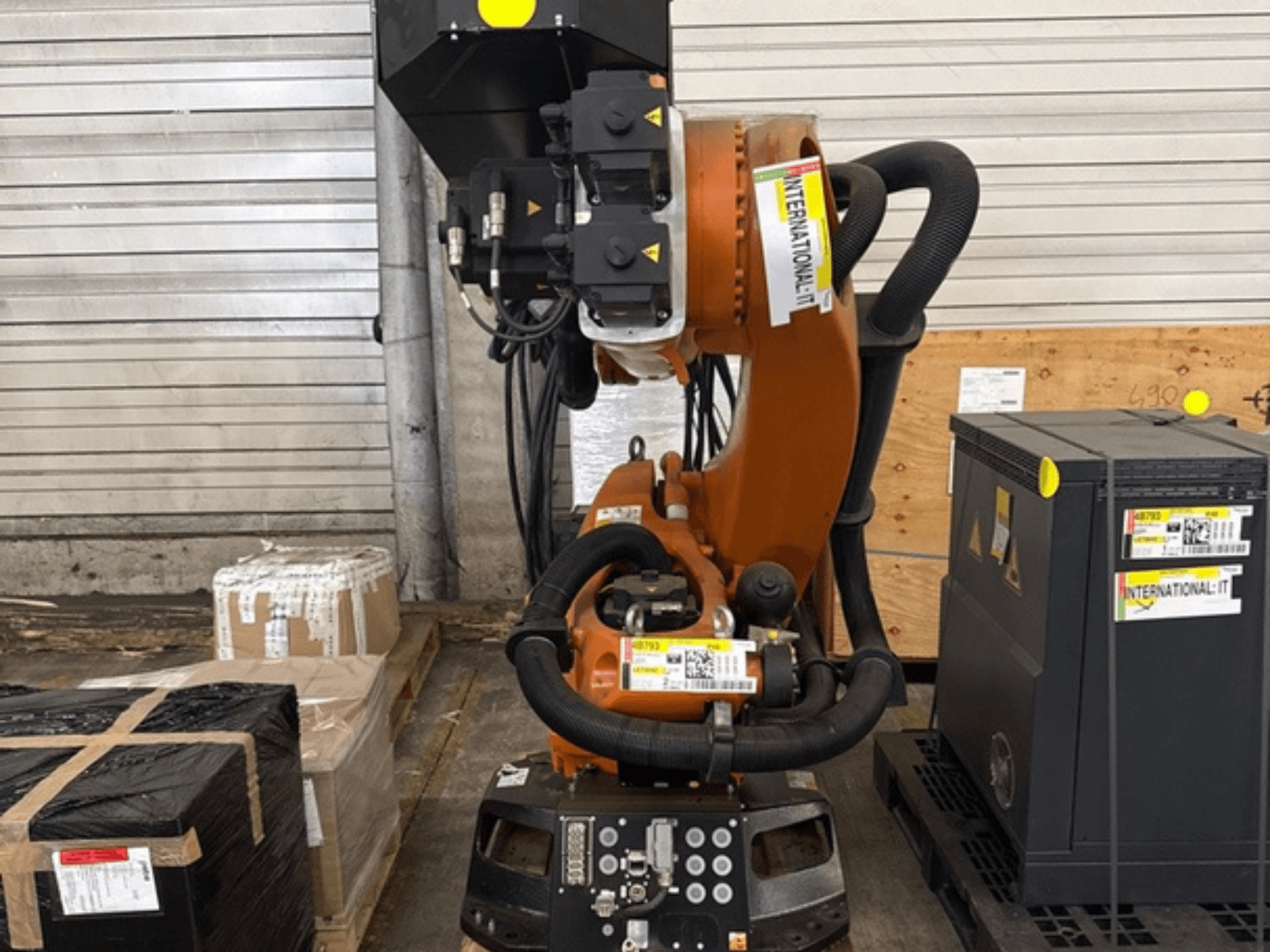 A KUKA KR 210 R2700 extra robotkar elölnézetben, egy raklapon csomagok és berendezések mellett kiállítva.