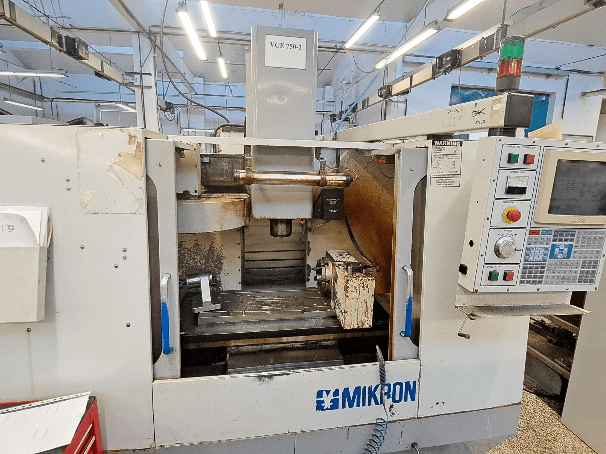 Mikron VCE 750-2 CNC marógép, elölnézet, a kezelőpanel és az orsó a megmunkálási területen, kopás és szennyeződés látható.