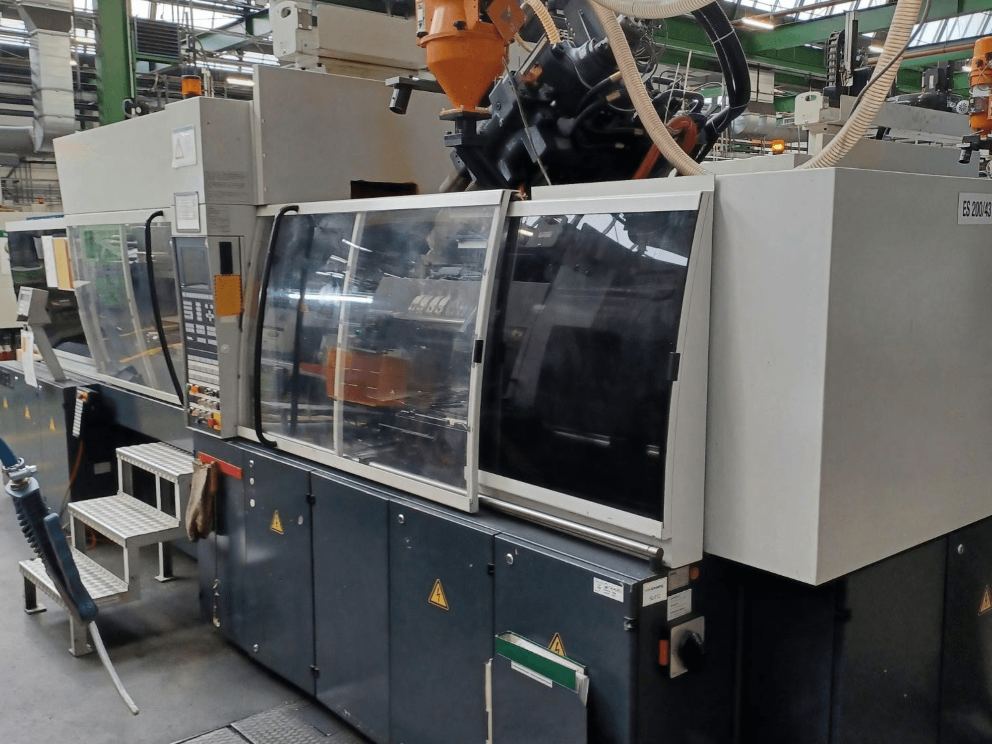 Egy műanyag fröccsöntőgép előlapja, márka és modell ismeretlen, átlátszó biztonsági ajtókkal és vezérlőpanellel.