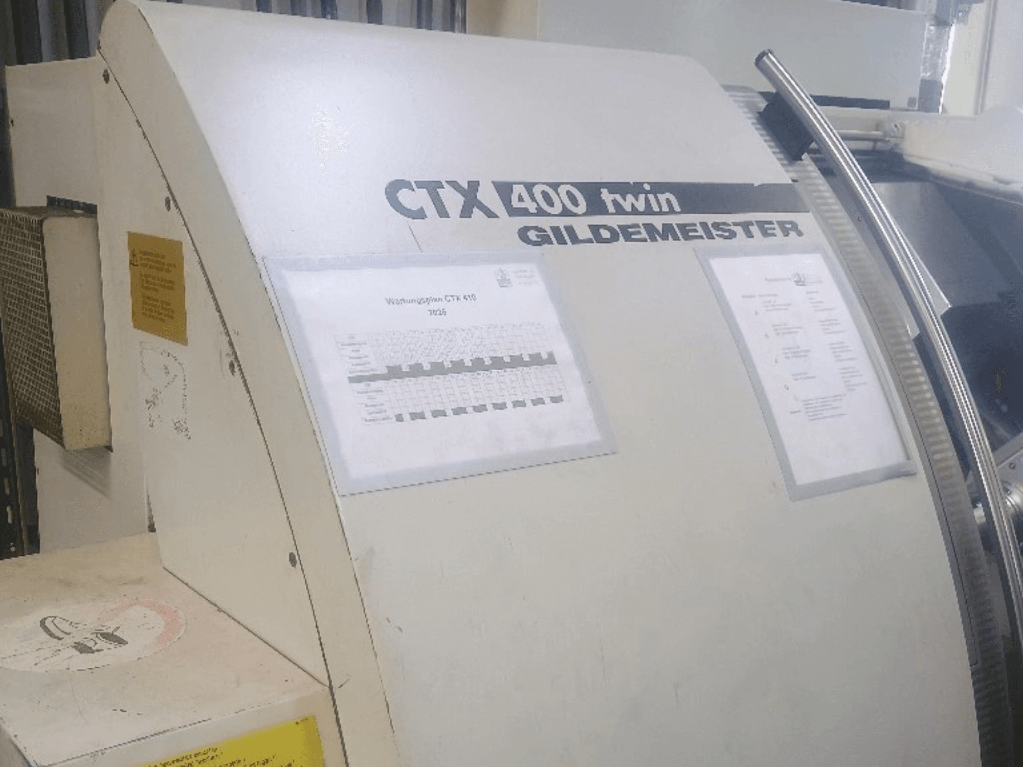 Gildemeister CTX 400 iker vízszintes eszterga, elölnézet, a kezelőpanelek és a műszaki dokumentáció látható.