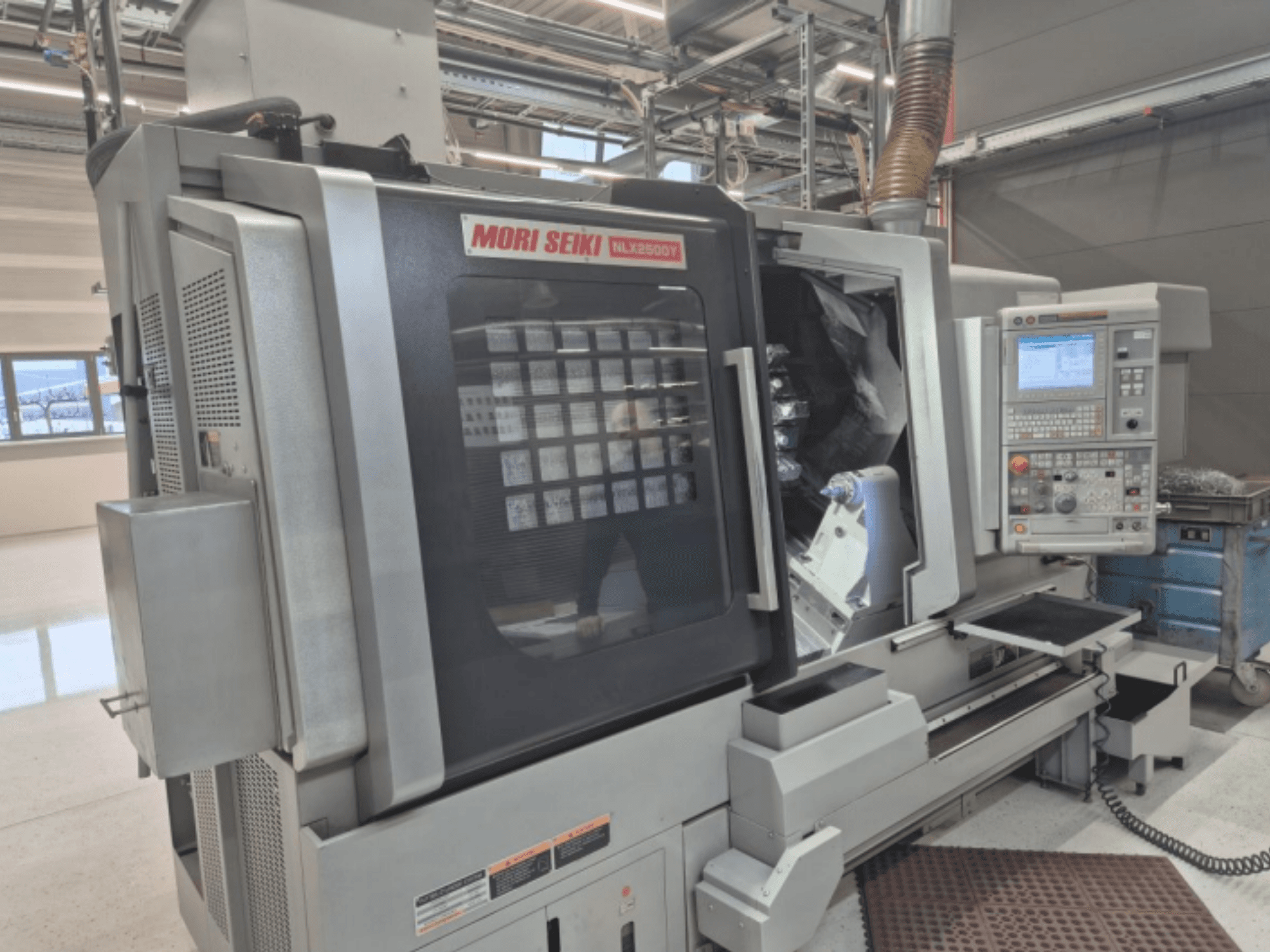 MORI SEIKI NL2500Y CNC esztergagép gyári beállításban, elölnézetben a vezérlőpanel és a munkadarabkamra.