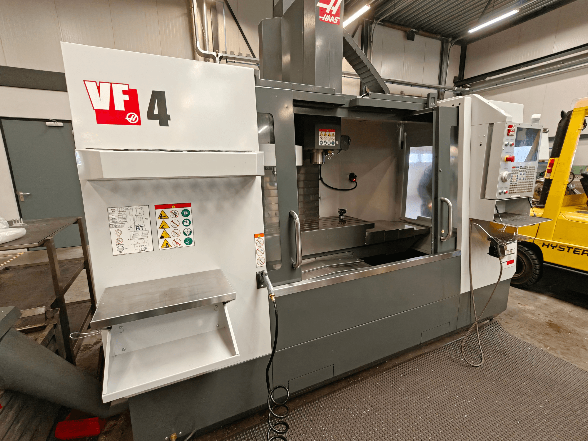 HAAS VF-4 függőleges megmunkálóközpont, elölnézet, a vezérlőpanel, a munkaterület és az oldalsó biztonsági címkék.